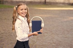 Girl cute schoolgirl hold book and headphones. audio book concept