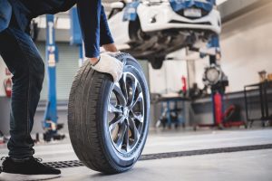 Male mechanic hold and rolling tire at repairing service garage background. Technician man replacing winter and summer tyre for safety road trip